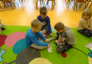Trzech chłopców ogląda ilustracje rozłożone na dywanie.